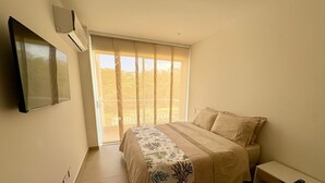 A bedroom with a bed, a TV mounted on the wall, a window with blinds, and a small bedside table. - Espacioso y Confortable Bai Kristal (Cartagena de Indias)