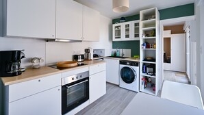 Una cucina compatta con mobili bianchi, forno integrato, macchina da caffè e lavatrice.