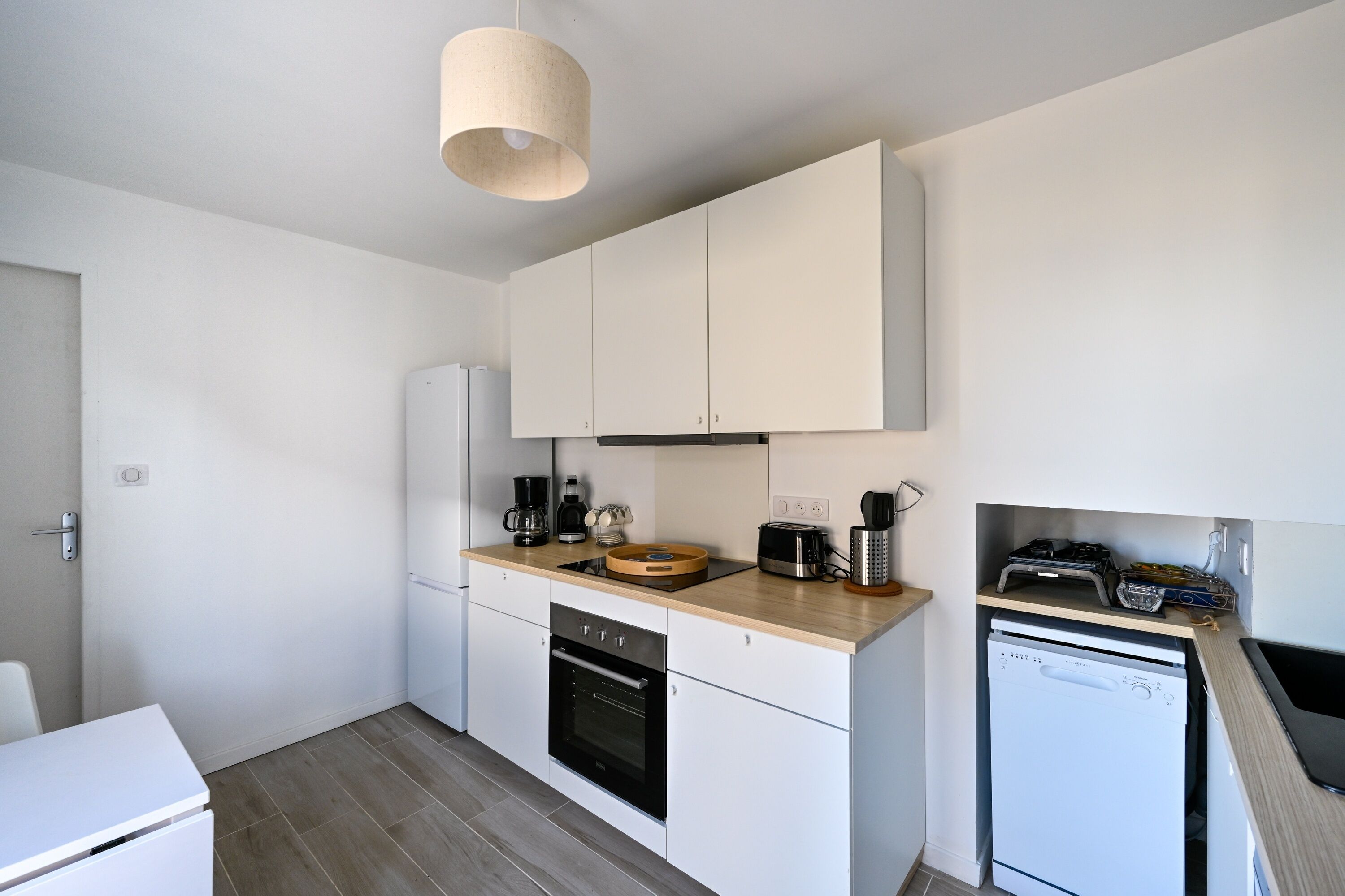 A modern kitchen with white cabinets, a built-in oven, a dishwasher, and a wooden countertop.