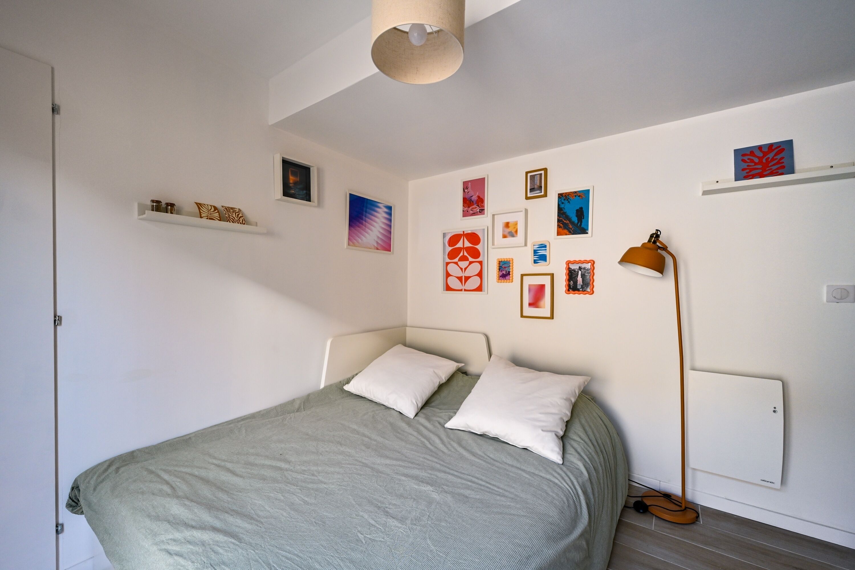 A bedroom with a bed, white walls, and various framed artworks.