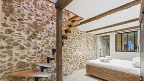 Een slaapkamer met een stenen muur, houten balken, een bed en een klein tafeltje.