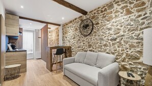 Een gezellige woonkamer met een stenen muur, een bank, een houten salontafel en een kleine eettafel met stoelen.
