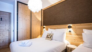 A modern bedroom with a wooden headboard, a large fluffy light fixture, and neatly made beds. - Les Chalets de L'Aiguille B101 (Le Grand Bornand)