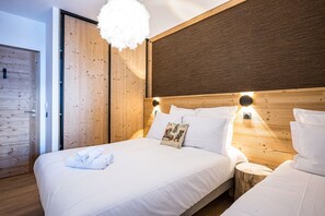 Ein modernes Schlafzimmer mit einem Holzkopfteil, einer großen, flauschigen Leuchte und ordentlich bezogenen Betten.