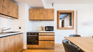 A modern kitchen with wooden cabinets, a built-in oven, and a dining area with a wooden table and chairs. - Les Chalets de L'Aiguille B101 (Le Grand Bornand)