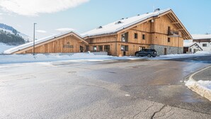 A wooden lodge with a sloped roof, a stone foundation, and a car parked in front. - Les Chalets de L'Aiguille B101 (Le Grand Bornand)