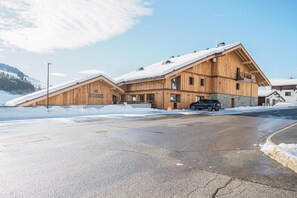 Eine Holzhütte mit geneigtem Dach und Steinfundament, davor ein geparktes Auto.