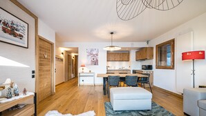 A modern living room with a white sofa, a dining area with a wooden table, and a kitchen with wooden cabinets. - Les Chalets de L'Aiguille B101 (Le Grand Bornand)
