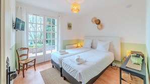 A bedroom with two beds, a chair, a TV, and a door leading to a balcony.
