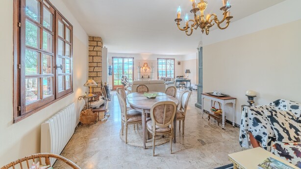 A spacious dining area with a round table and chairs, a chandelier, and a view of the kitchen in the background.