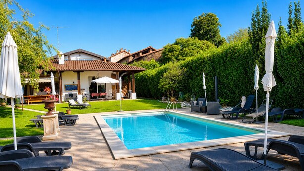 A swimming pool with lounge chairs and umbrellas, surrounded by a well-maintained lawn and a building with a tiled roof. - Ai4soli di Cermenate (Cermenate)