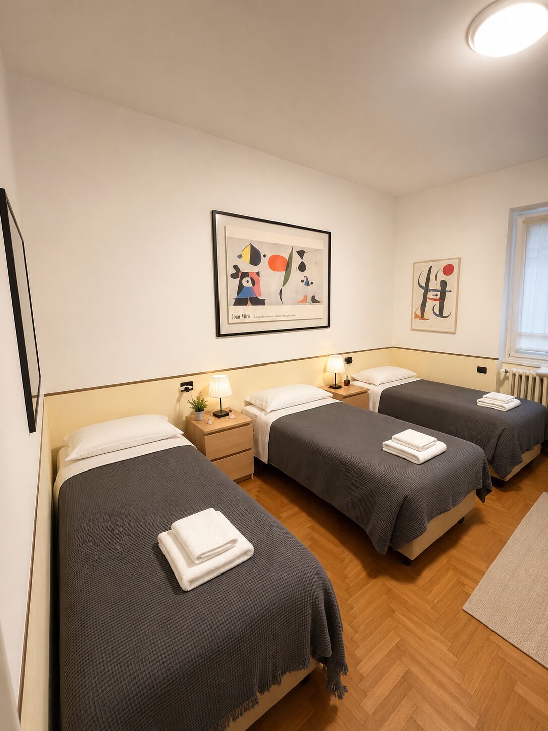 Une chambre d’hôtel avec trois lits, un plancher en bois et deux œuvres d’art accrochées au mur.