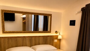A hotel room with a bed, two pillows, a nightstand, a lamp, a mirror, and a TV. - Ai4soli di Cermenate (Cermenate)