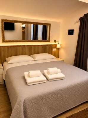 Ein Hotelzimmer mit Bett, zwei Kissen, einem Nachttisch, einer Lampe, einem Spiegel und einem Fernseher.
