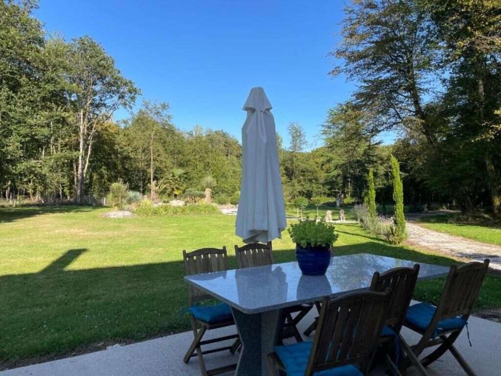 Un patio al aire libre con una mesa y sillas de vidrio, rodeado por un exuberante jardín y árboles.