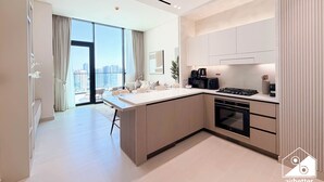 A modern kitchen with a central island, built-in appliances, and a large window offering a city view. - Binghatti Phantom Bliss 1BR With Private Pool (Dubai)