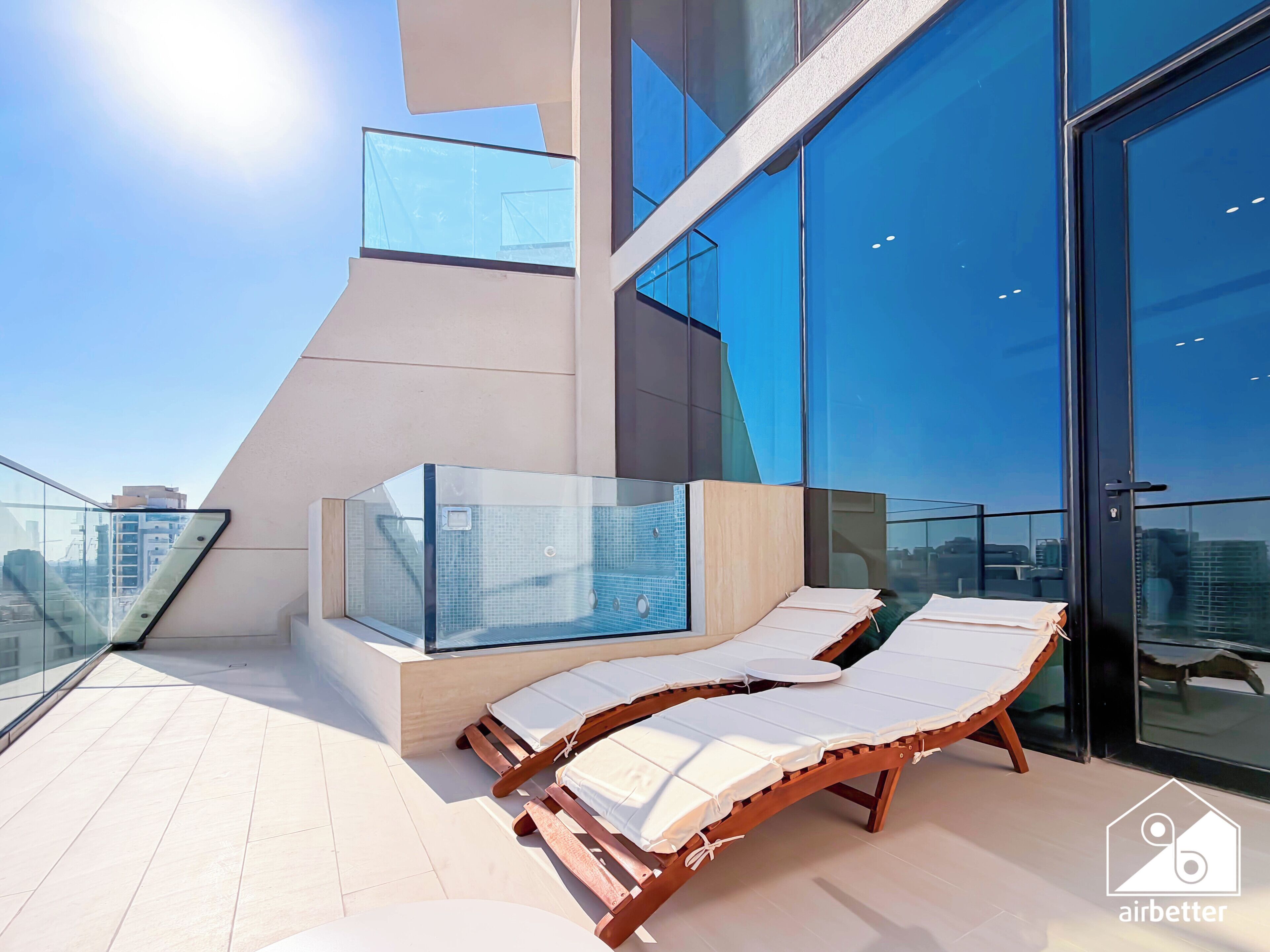 A modern rooftop terrace with glass balustrades, wooden lounge chairs, and a clear view of the city skyline.
