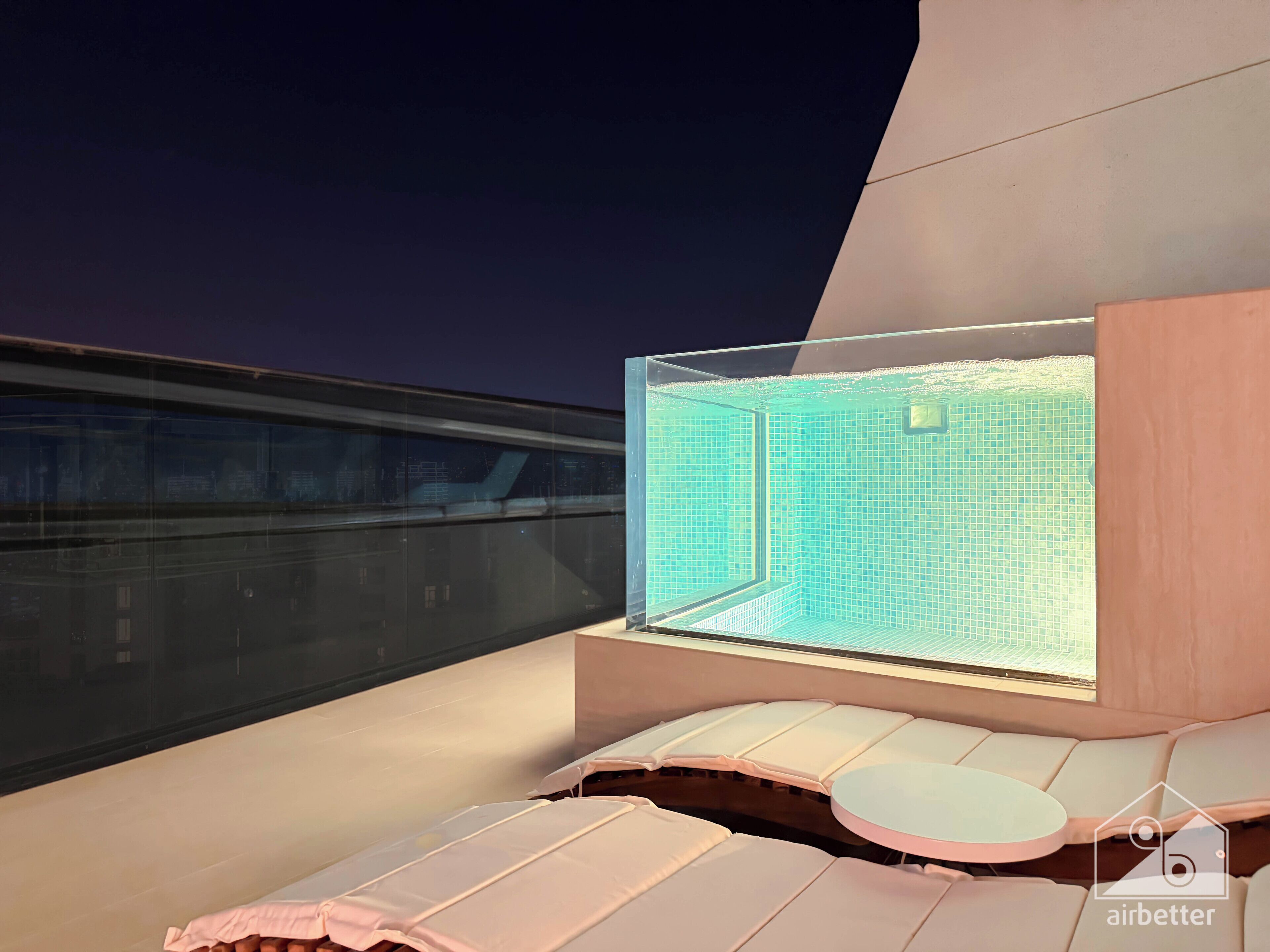 A modern lounge area with a pool view, cushioned seating, and a glass partition.