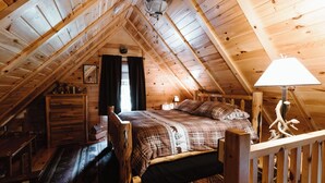 Ein gemütliches Schlafzimmer im Dachgeschoss mit Holzbalkendecke, einem Bett mit karierter Bettwäsche, einem Nachttisch und einer Lampe.
