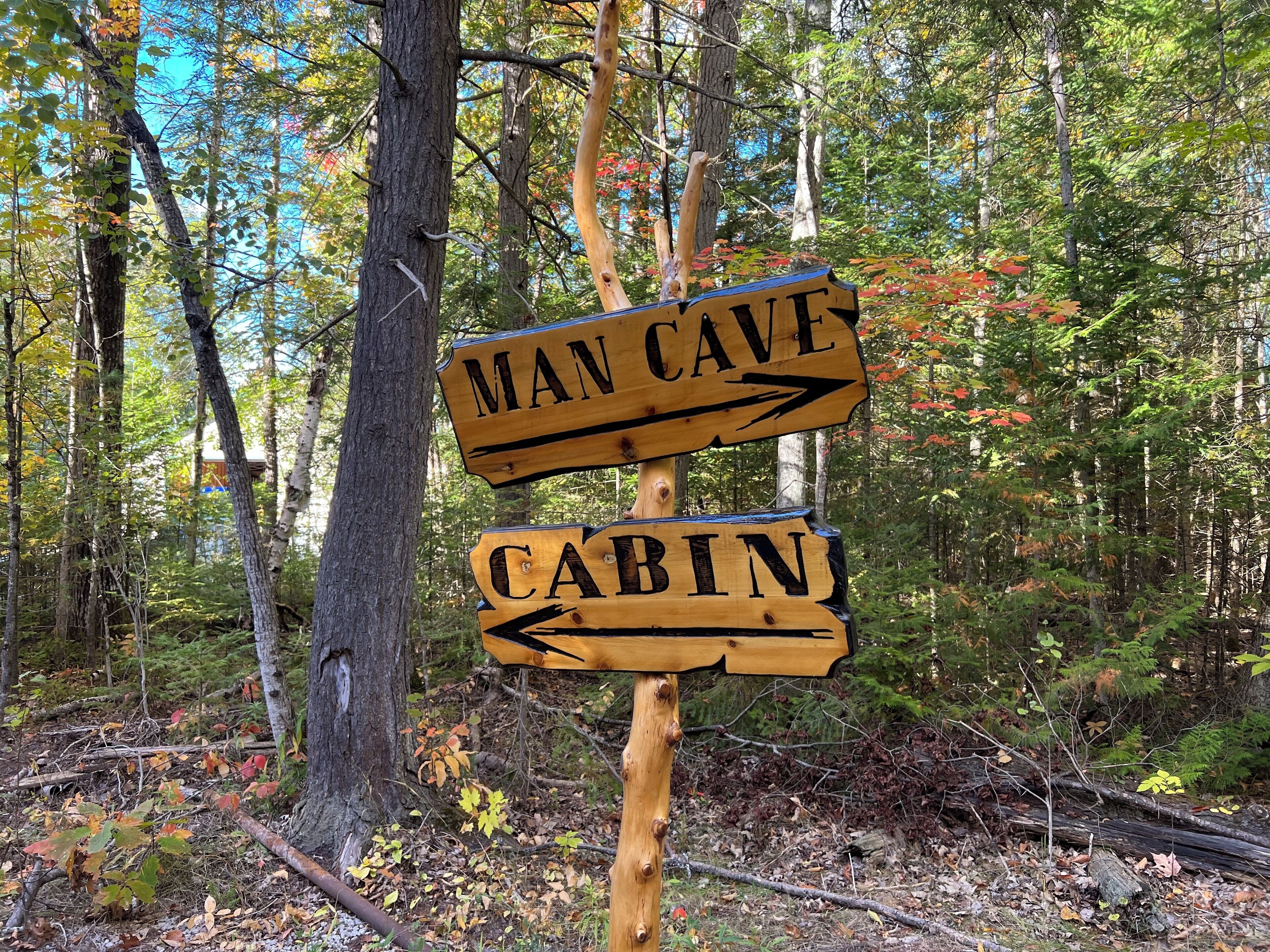 A wooden directional sign in a forest, pointing to 'Man Cave' and 'Cabin'.