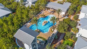 Vista aérea de un resort con una piscina central rodeada de palmeras y sillas de descanso.