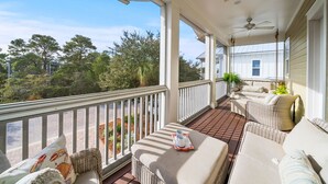 Un porche cubierto con mobiliario de mimbre, un ventilador de techo y vistas del paisaje circundante.