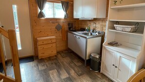 A compact kitchen with wooden walls, a sink, cabinets, and a window with curtains.