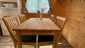 A wooden dining table with chairs, a window with curtains, and a plant on the wall.