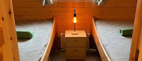 Una cabaña con dos literas, una mesita de noche pequeña con una lámpara y una ventana con cortinas.