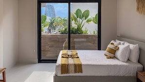 A modern bedroom with a large bed, a view of a cityscape, and a balcony with plants. - Almare by Andiani Travel (Cancun)