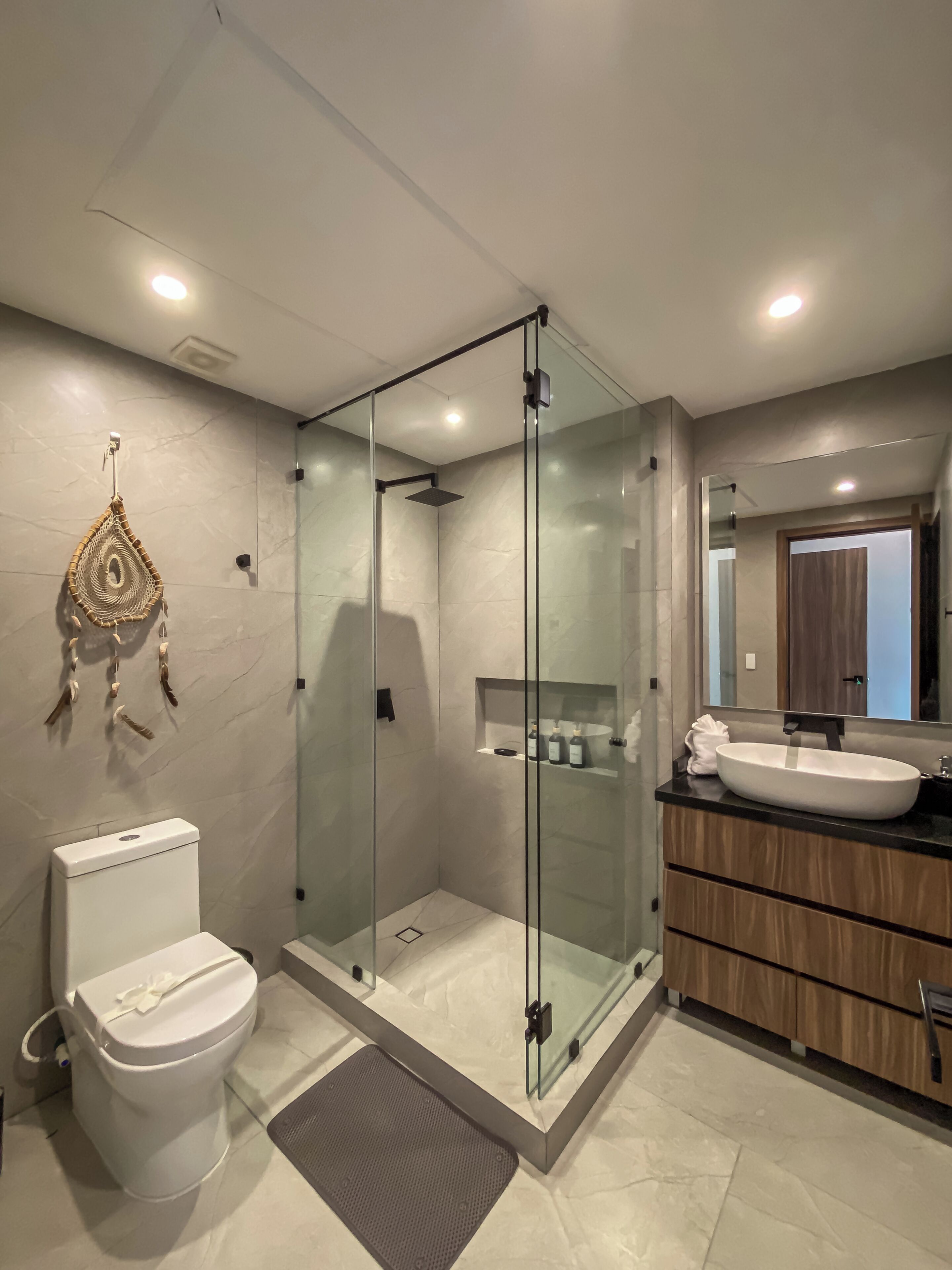 Une salle de bain moderne avec une douche à parois de verre, des toilettes blanches et un meuble-lavabo doté d’un grand miroir.