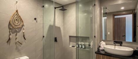 Une salle de bain moderne avec une douche à parois de verre, des toilettes blanches et un meuble-lavabo doté d’un grand miroir.