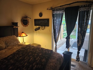 Un dormitorio con cama, mesita de noche con lámpara, reloj de pared y ventana con cortinas.