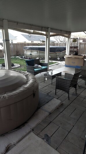 Ein überdachter Patio-Bereich mit Whirlpool, Gartenmöbeln und Feuerstelle.
