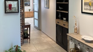 A modern interior with a staircase, a brick wall, and a hallway leading to a room with a desk and shelves.