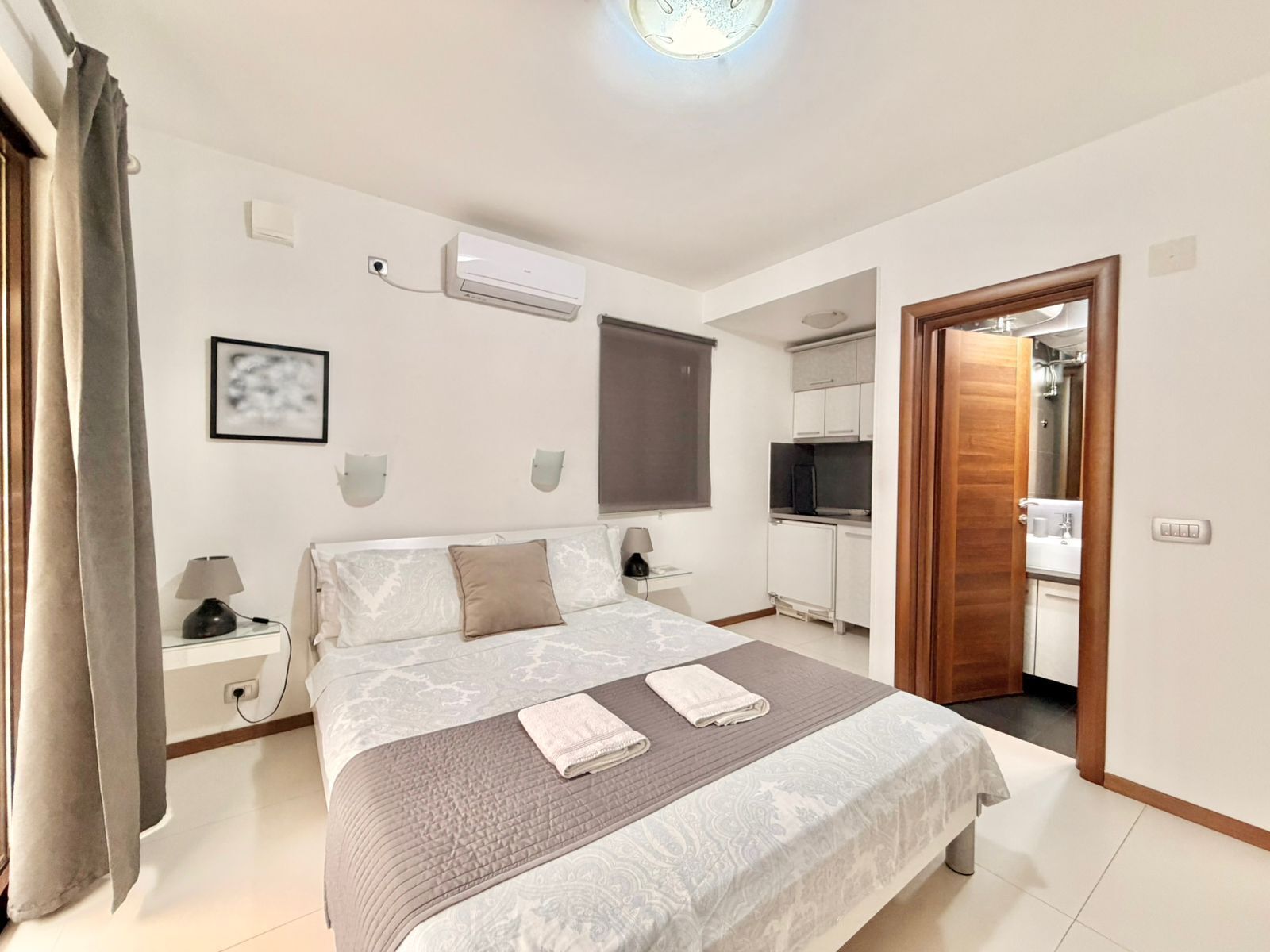 A bedroom with a large bed, bedside tables, a TV, a wardrobe, and a bathroom visible through an open door.