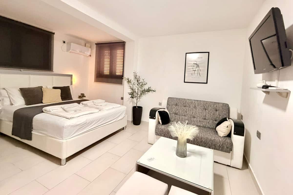 A modern hotel room with a bed, a sofa, a coffee table, a TV, and a framed picture on the wall.