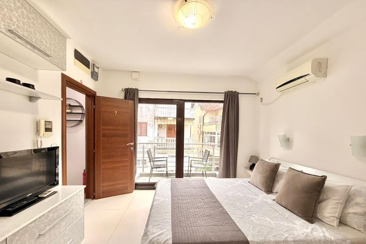 A hotel room with a bed, a TV, a dresser, and a balcony with a view of buildings.