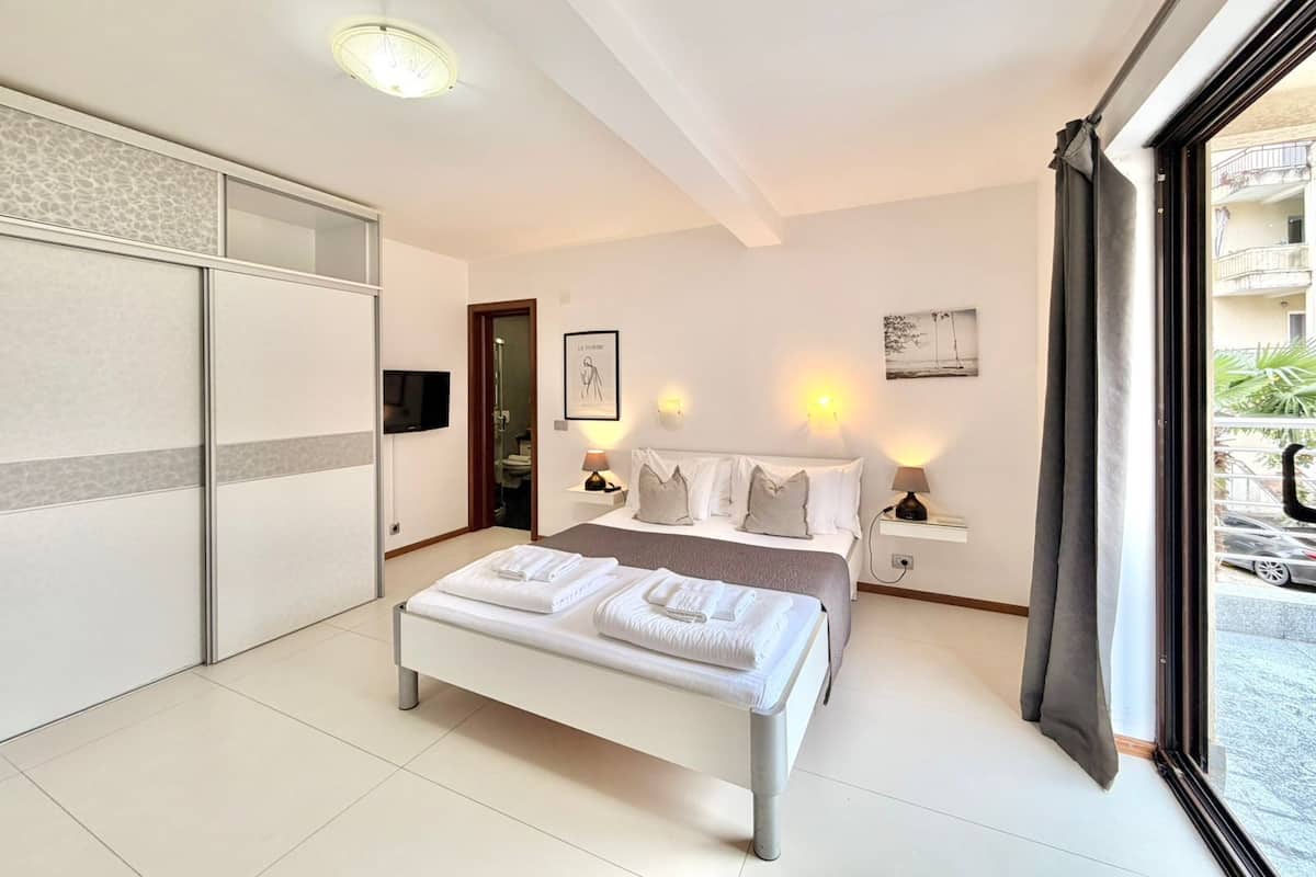 A modern bedroom with a bed, bedside tables, a TV, and a view of the outside.