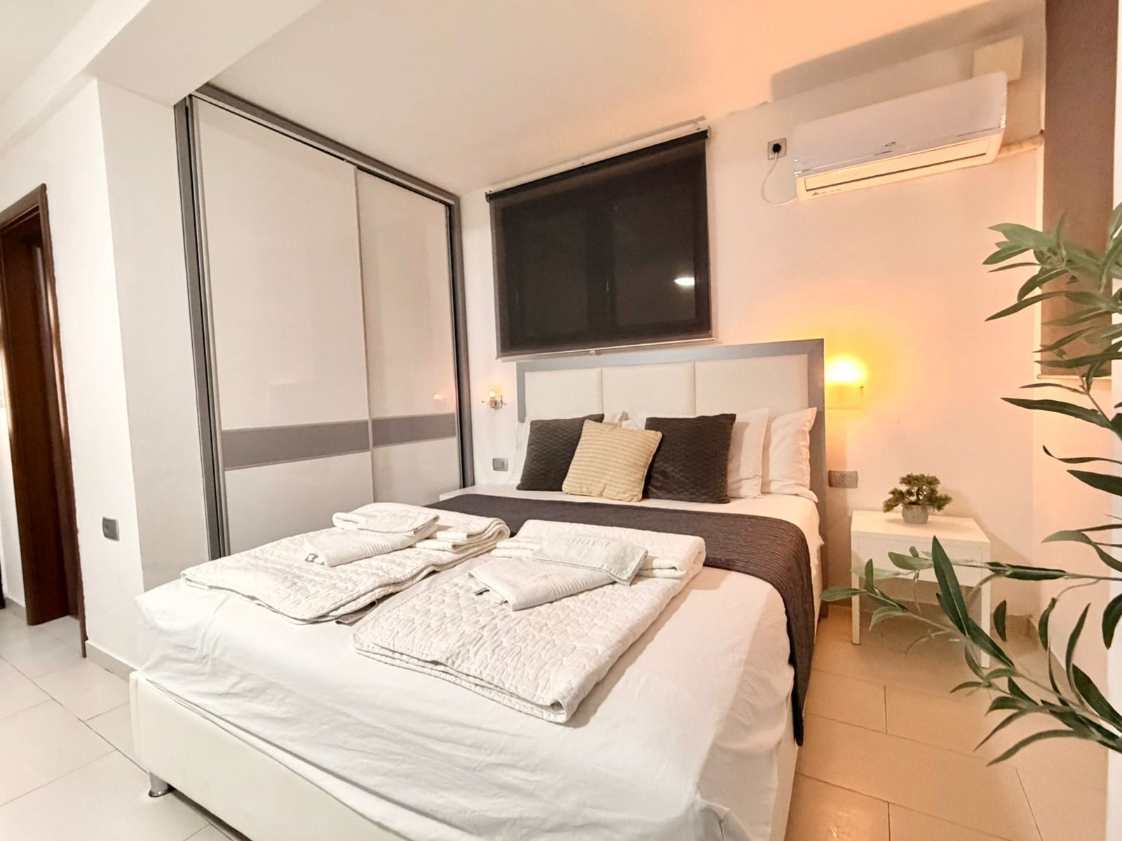 Un dormitorio moderno con una cama grande, un televisor montado encima y un aire acondicionado en la pared.
