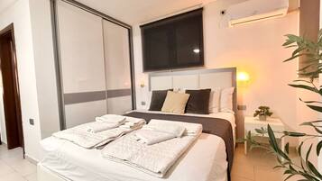 Un dormitorio moderno con una cama grande, un televisor montado encima y un aire acondicionado en la pared.