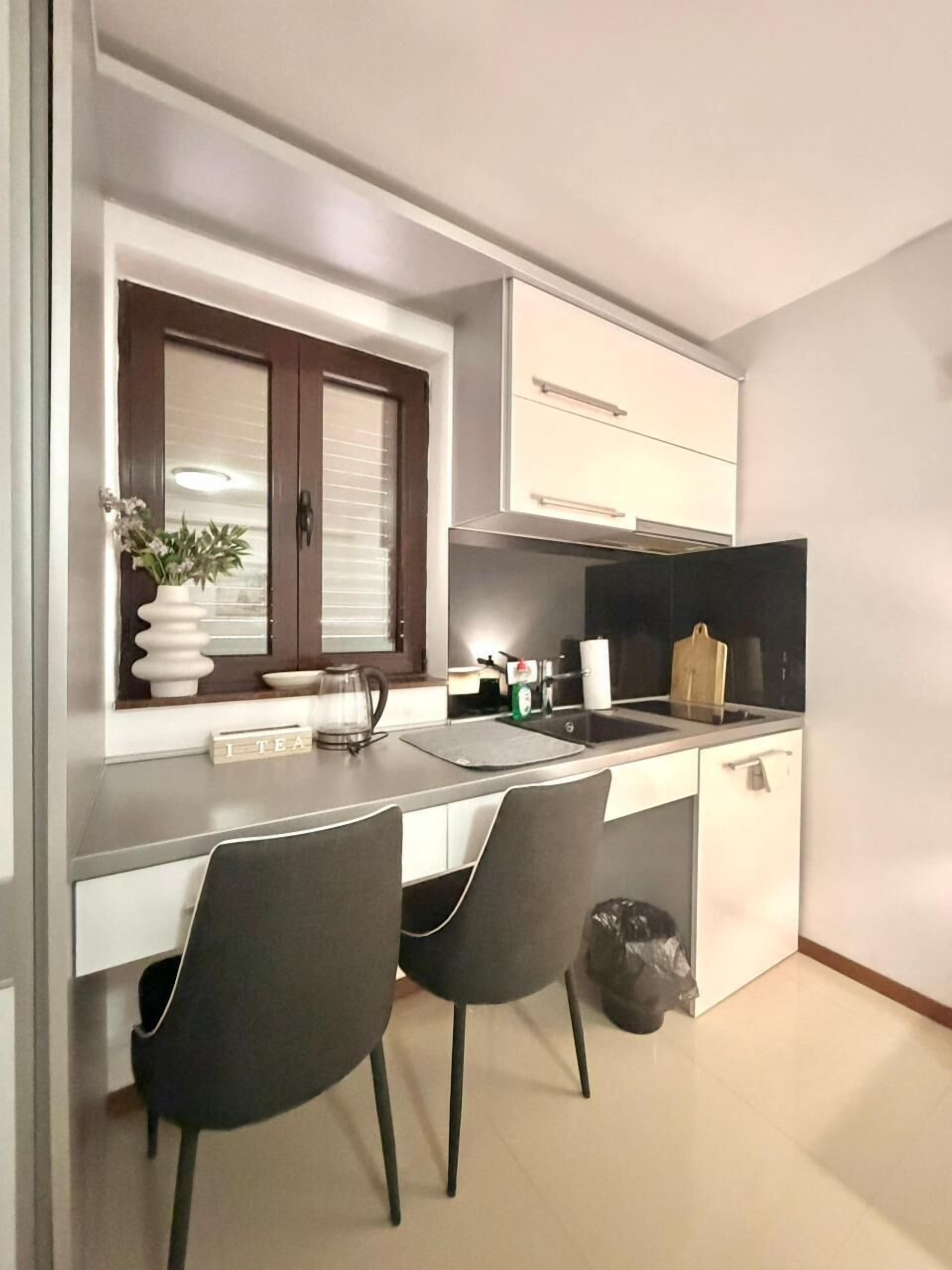 A compact kitchen with a window, a sink, two chairs, and a trash bin.