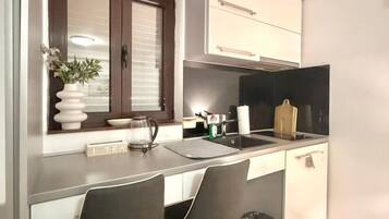 A compact kitchen with a window, a sink, two chairs, and a trash bin.