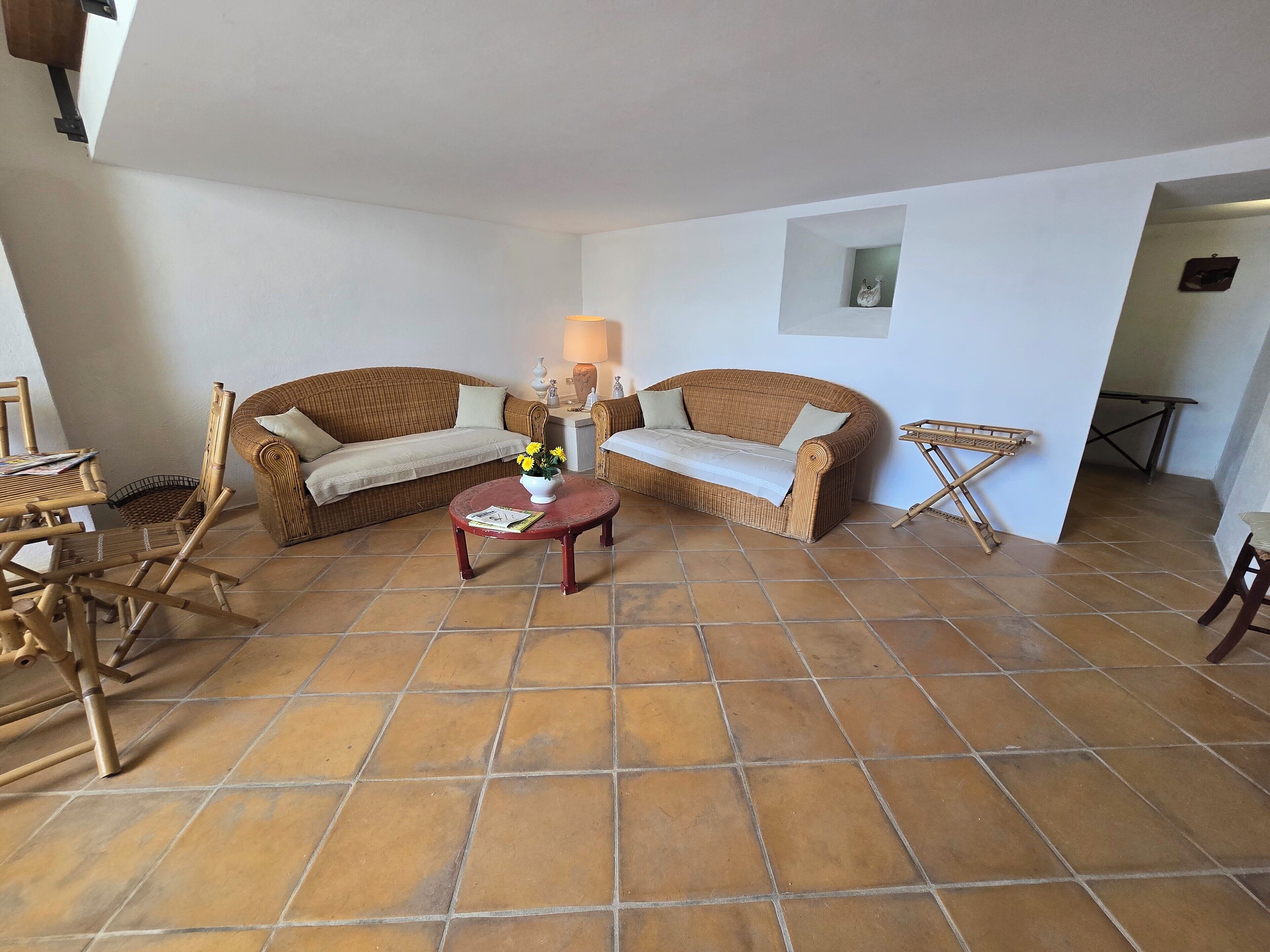 A living room with a brown wicker sofa, a small red table, and a wicker chair.