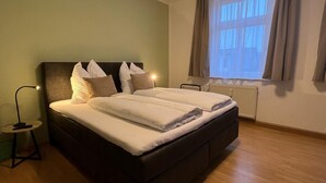 Un dormitorio con una cama grande, una mesita de noche con lámpara, una ventana con cortinas y un radiador.