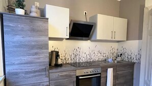 Una cocina moderna con armarios grises, horno empotrado, microondas y un televisor de pantalla plana sobre el lavamanos.