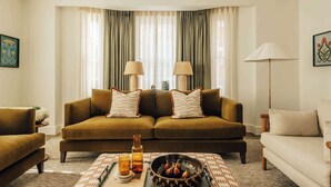 A living room with a brown sofa, two lamps, a coffee table with a bowl of figs, and a floor lamp. - Mayfair Luxury 3BR at SLO Claridge House (London)