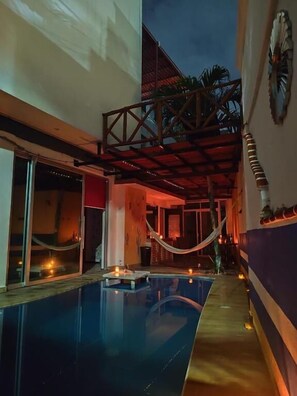 Una piscina interior con estructura de techo de madera, una hamaca y velas.