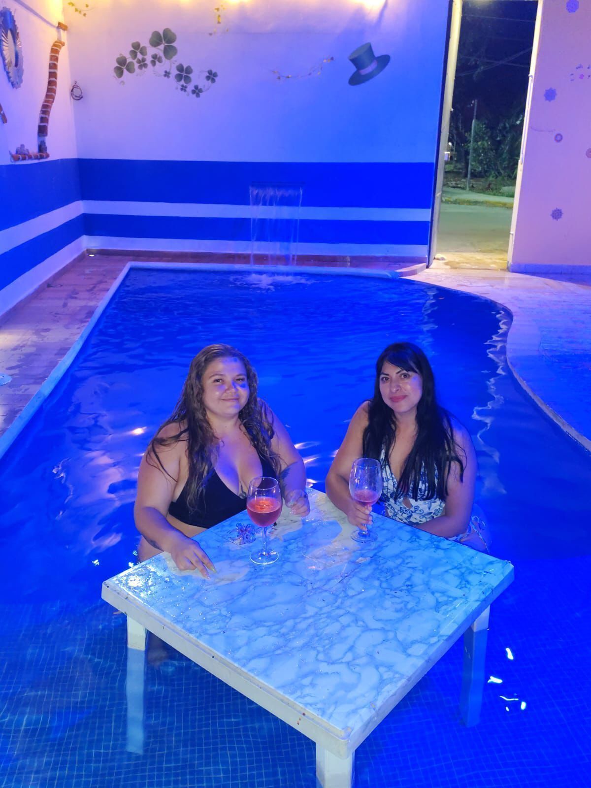 Two people seated at a table by a pool with a blue and white color scheme and decorative wall art.