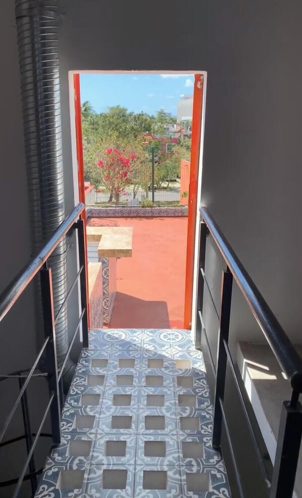 Una escalera con piso estampado que conduce a un espacio exterior con un muro rojo y un árbol con flores rosadas.